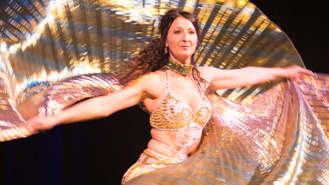 Ein Tänzerin in goldenem Kostüm zeigt eine Tanzfigur.