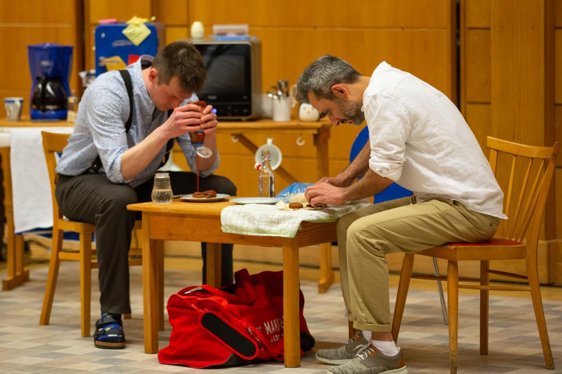 Zwei junge Männer sitzen an einem Küchentisch und bereiten Essen zu.