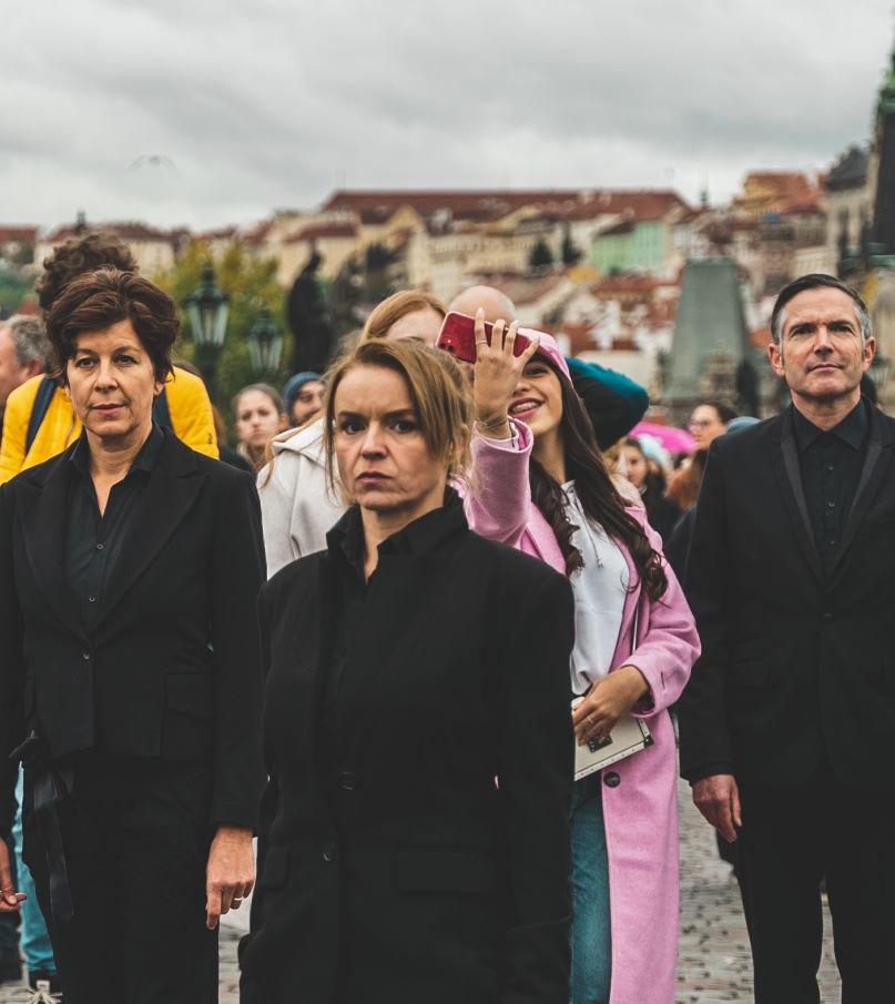 Mehrere schwarzgekleidete Personen stehen inmitten einer Touristenmenge auf einer Brücke in Prag.
