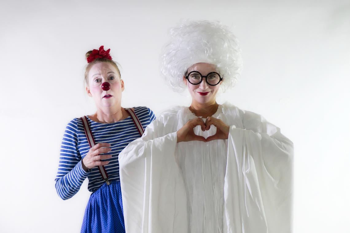 Ein weißes Gespenst zeigt das Herz-Zeichen mit den Händen, hinter ihm steht eine Clownin mit roter Nase.