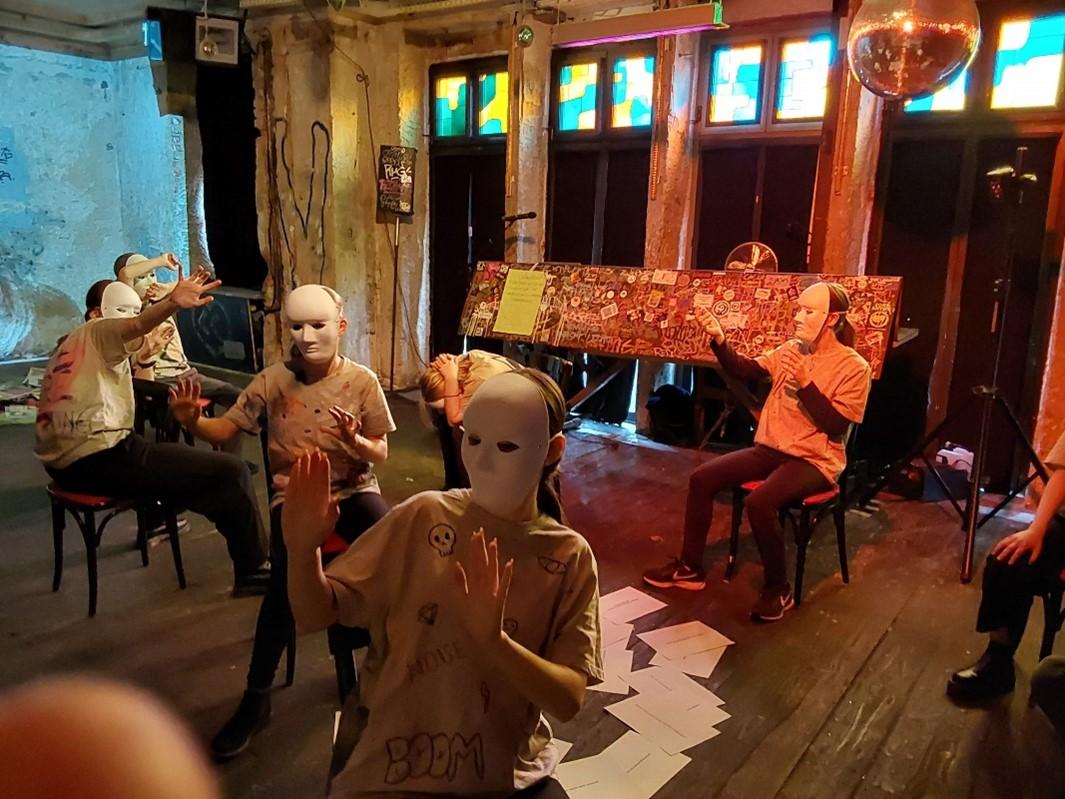 Eine Gruppe maskierter Personen bewegt sich über eine Bühne.