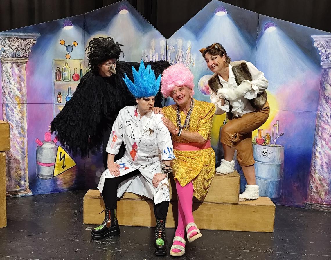 Ein Zauberer und eine Hexe sitzen in einem Labor, umrahmt von einem Raben und einer Katze.