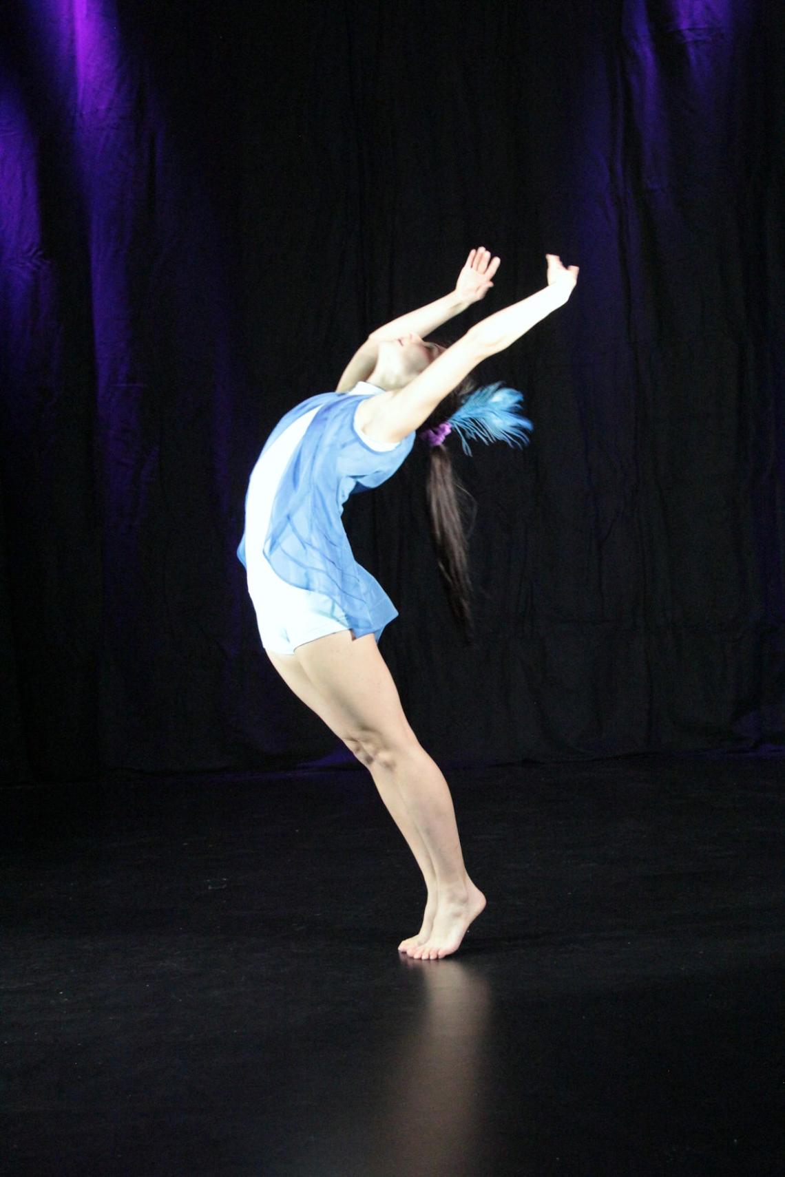 Eine Tänzerin in einem blauen Trikot bewegt sich auf einer Bühne.