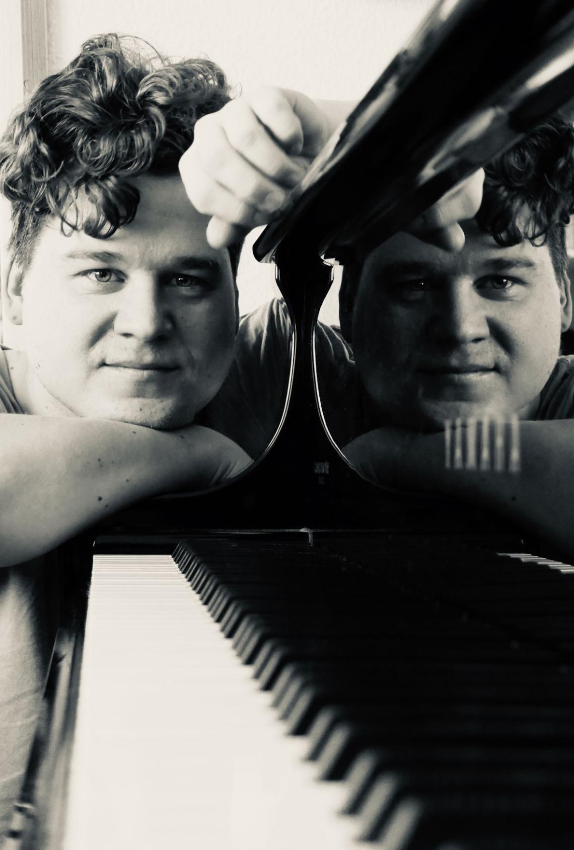 Ein Pianist spiegelt sich im Lack eines Konzertflügels.