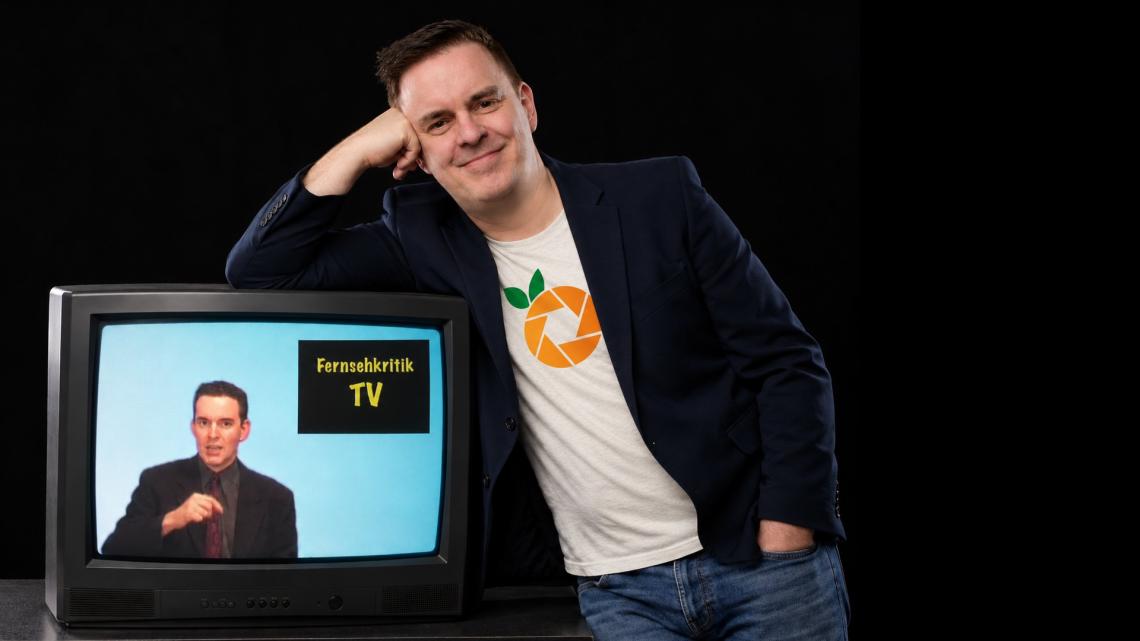 Ein Mann lehnt lässig auf einem Fernseher.