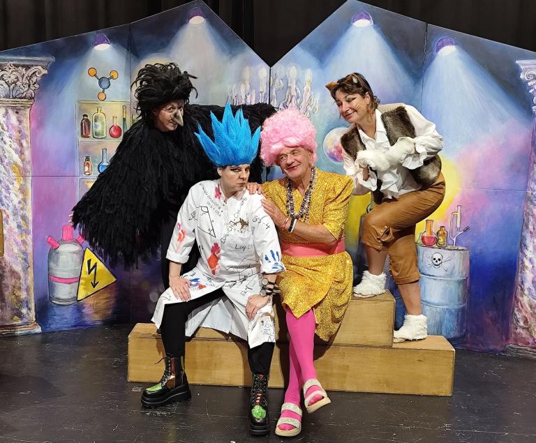 Ein Zauberer und eine Hexe sitzen in einem Labor, umrahmt von einem Raben und einer Katze.