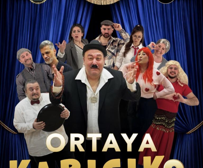 Ein Mann im schwarzen Anzug steht vor einem Theatervorhang, umgeben von vielen Figuren in diversen Kostümen.