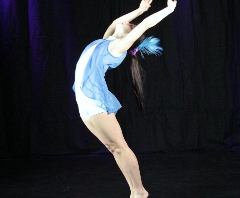 Eine Tänzerin in einem blauen Trikot bewegt sich auf einer Bühne.