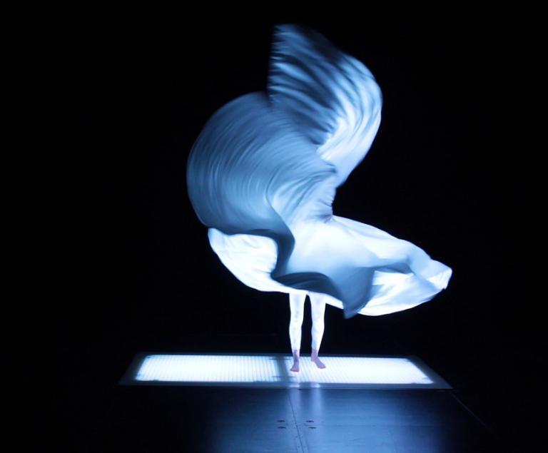 Eine Tänzerin steht mit weit schwingendem Kleid in blauem Licht.