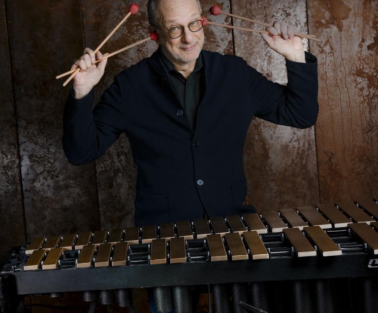 Ein Vibraphonspieler steht hinter seinem Instrument und hält sich die Schlegel in einer lustigen Geste an die Ohren.