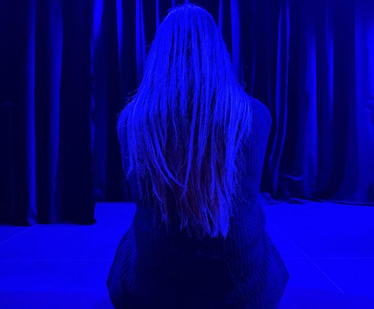 Eine junge Frau sitzt in einem Raum voll blauem Licht.