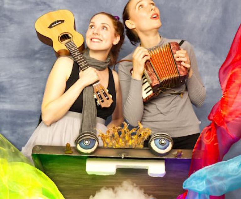 Zwei junge Frauen mit Musikinstrumenten und einem Koffer mit Augen, aus dem Farben sprühen.