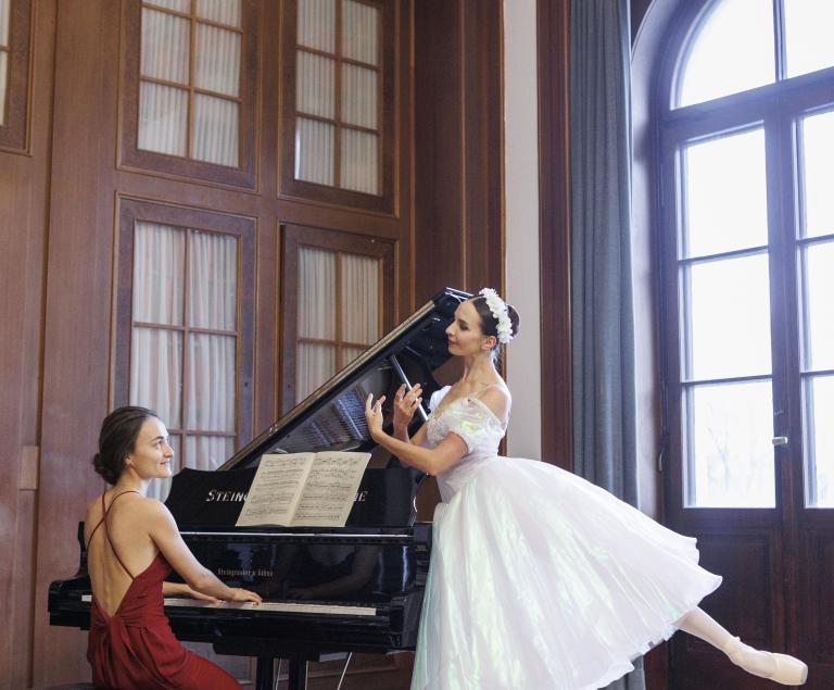 Eine Pianistin sitzt am Flügel, während neben ihr eine Ballerina tanzt.