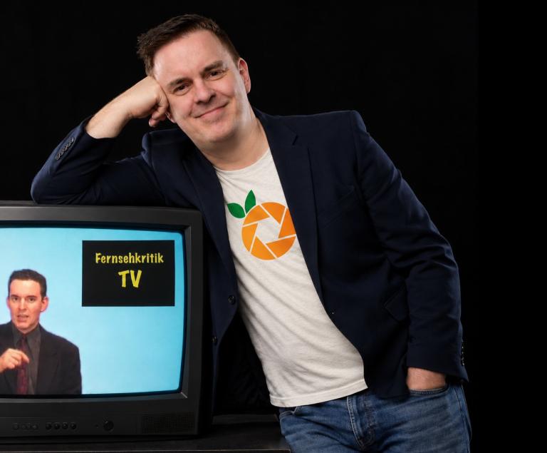 Ein Mann lehnt lässig auf einem Fernseher.